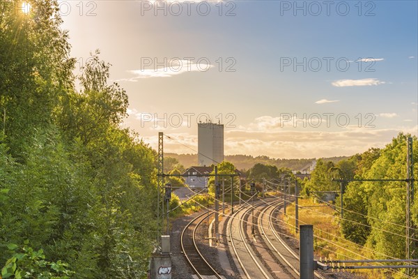 Landscape with the sun rays passing through the green trees and enlightening the railways and the industrial buildings that lies on the horizon