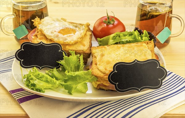 Plate with sandwiches, fried egg, tomato and green salad on wooden table. Each sandwich has a blank paper tag for short messages