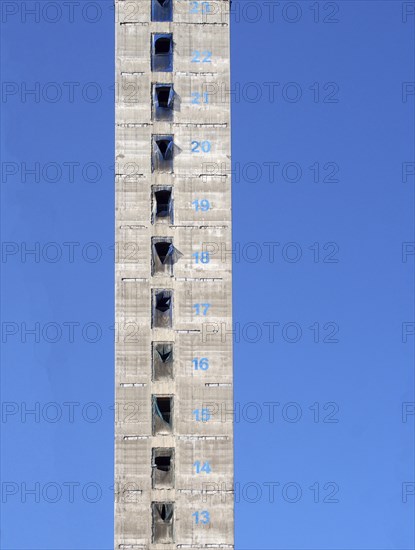 A tall concrete structure and service core of a new skyscraper building under construction with floor numbers marked in paint against a blue sky