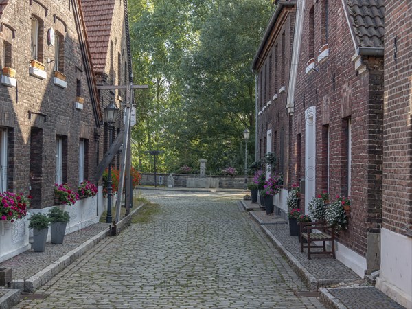 Quiet, cobbled alley with brick houses and potted plants, surrounded by trees, old-town atmosphere, krudenburg, hünxe, lower rhine, germany