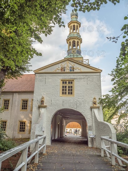 Tor tor with church tower above and decorative elements, offering a view of a building complex and a pedestrian bridge, dornum, east frisia, germany