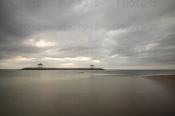 Beautiful seascape in the morning. Tropical sandy beach with breakwater and reflection of the sky in the calm water. Morning landscape, taken in Sanur, Bali, Indonesia, Asia