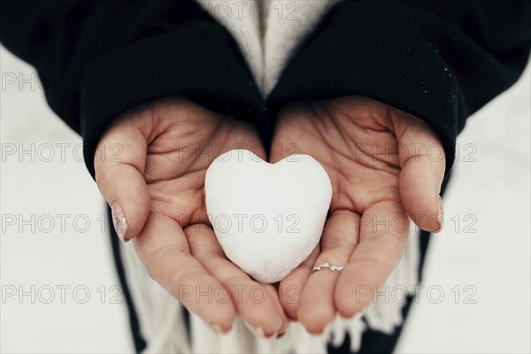 Snow heart snowball in girl gloved hands. Blurred background.