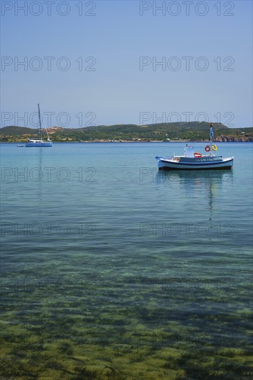 Greek fishing boat moored in blue waters of Aegean sea in harbor of near Milos island, Greece, Europe