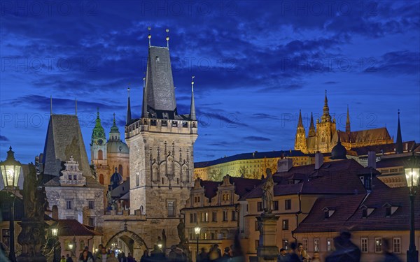 Blue hour view of illuminated landmark Lesser Town Charles Bridge gothic tower and historic buildings under a deep blue sky, Prague, Czech Republic, Europe