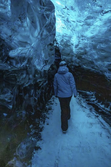 A woman is walking through a blue cave. The cave is illuminated by blue light, creating a serene and peaceful atmosphere