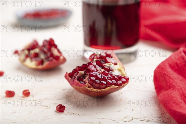 Glass of pomegranate juice on a white concrete background with red textile. Side view, close up, selective focus