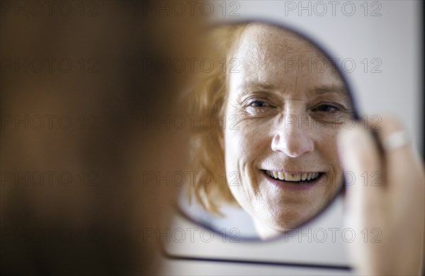 Symbol photo. A smiling elderly woman can be seen in a mirror. Berlin, 13.08.2024