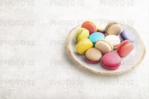 Multicolored macaroons on ceramic plate on gray concrete background. side view, close up, still life, copy space. Breakfast, morning, concept