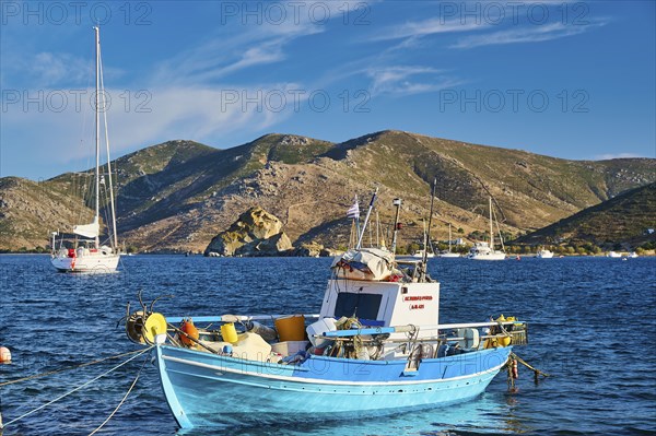 Colourful fishing boat on blue water, with mountains and cloudy sky in the background, Petras Beach, Kalikatsou Rocks, Patmos, Dodecanese, Greek Islands, Greece, Europe