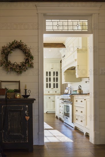 White painted maple wood antique style cabinets with tan coloured quartz countertops in kitchen with stained oak wood floorboards inside country style home, Quebec, Canada, North America