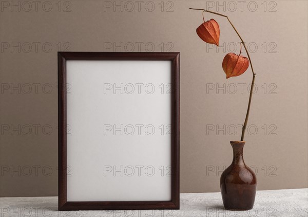 Brown wooden frame mockup with physalis in ceramic vase on beige paper background. Blank, vertical orientation, still life, copy space