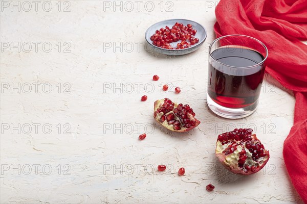 Glass of pomegranate juice on a white concrete background with red textile. Side view, copy space, close up