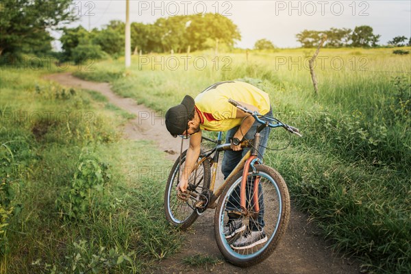 Man repairing his bike in the middle of the road. Man in the countryside repairing his bike