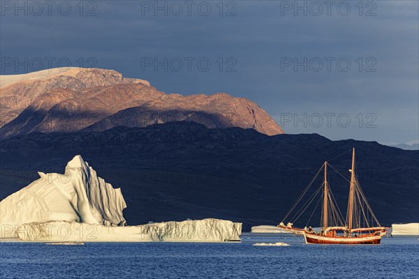Sailing boat, ship in fjord in front of large icebergs and mountains, evening light, Scoresby Sound, East Greenland, Greenland, North America