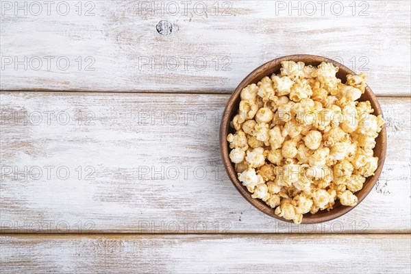 Popcorn with caramel in wooden bowl on a white wooden background. Top view, flat lay, copy space