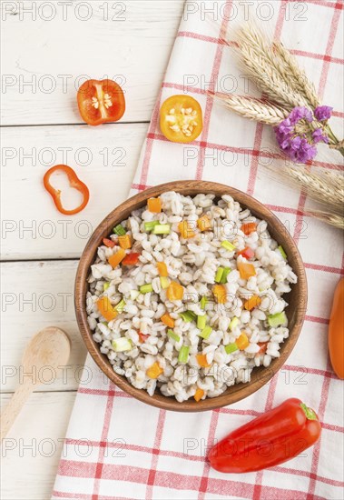 Pearl barley porridge with vegetables in wooden bowl on a white wooden background and linen textile. Top view, flat lay, close up. Russian traditional cuisine