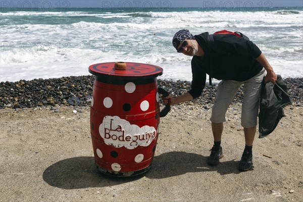 Red outdoor bar table, hiker, tourist holding jug, bar, beach bar, Cabo de Gata Natural Park, Cabo-de-Gata-Nijar, Las Negras, Almeria, Andalusia, Spain, Europe