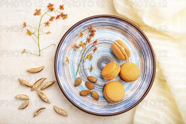 Orange macarons or macaroons cakes with cup of coffee on a white concrete background and linen textile. Top view, flat lay, close up