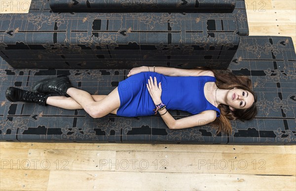 Portrait of an 18 year old white woman, in a blue short dress, lying on a grey couch, view from above, Brussels