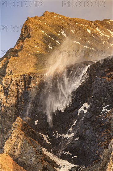 The spray of a waterfall sprays upwards, strong wind, mountains, morning light, East Iceland, Iceland, Europe