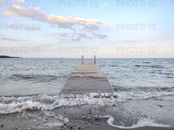 Wooden jetty leads into the sea at sunset, with calm waves and a pastel-coloured sky