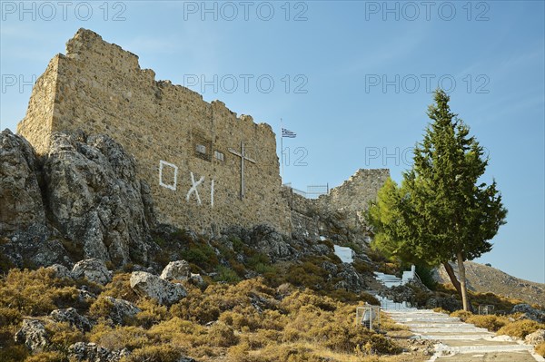 Stone ruin with cross on a hill, stairway and Greek flag under a clear sky, St John's Castle, Oxi Graffiti, Archengelos village, Rhodes, Dodecanese, Greek Islands, Greece, Europe