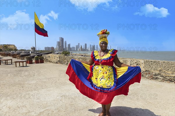 Cartagena, Colombia, 8 May, 2024: Colombia, lady in national colorful costume posing in Walled City historic center of Cartagena near Colombian flag, South America