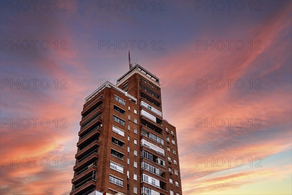 Madrid, Spain, October 16, 2021: Low angle view of old residential skyscraper against colorful sunset sky. Brick building, Space for copy, Europe