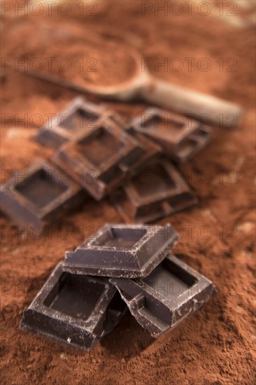 Presentation of some cubes of dark chocolate on a bed of cocoa