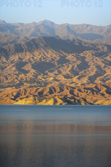 Blue Toktogul reservoir between dry mountain landscape, hilly mountains in the evening light, Jalalabad region, Kyrgyzstan, Asia