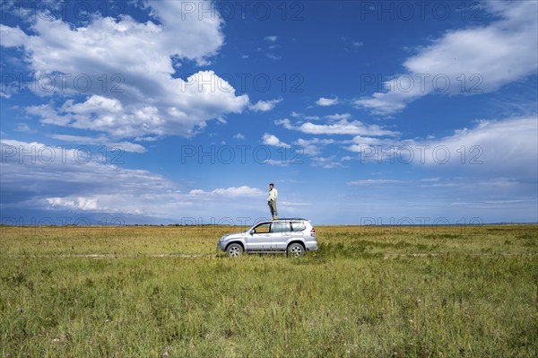 A man stands on a car in the centre of a vast landscape under a blue sky, Yssykköl, Kyrgyzstan, Asia