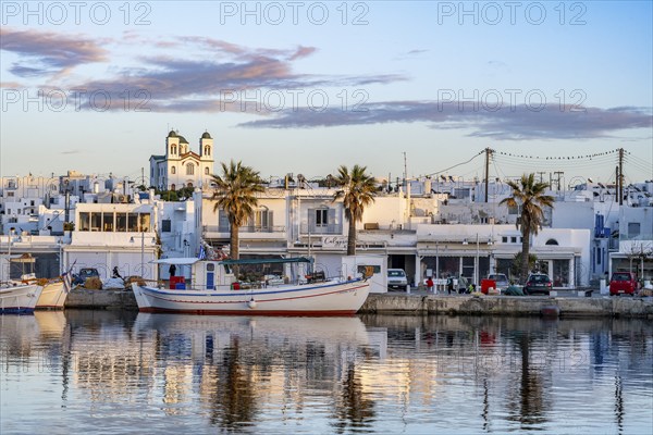 View of Naoussa, Fishing boats in the harbour at sunset, reflected in the sea, White Cycladic houses and church Agios Faneromeni, Naoussa, Paros, Cyclades, Greece, Europe
