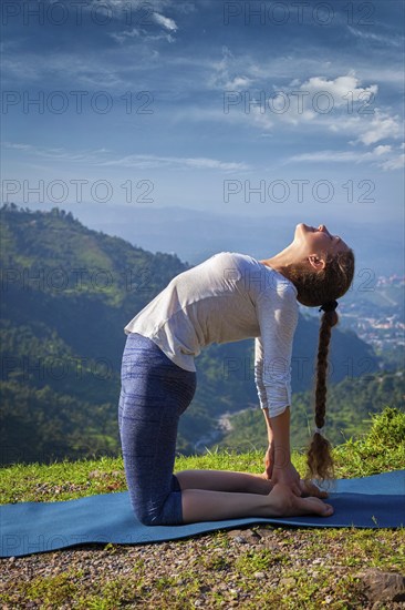Yoga, outdoors young beautiful slender woman yoga instructor doing camel pose Ustrasana asana exercise outdoors in mountains in the morning