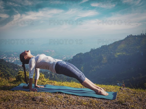 Woman doing Hatha yoga asana Purvottanasana plank pose outdoors in mountains. Vintage retro effect filtered hipster style image