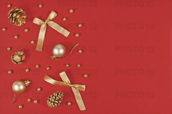 Christmas flat lay with elegant golden ornaments like tree baubles, painted pine cones and ribbons on side of red background with empty copy space