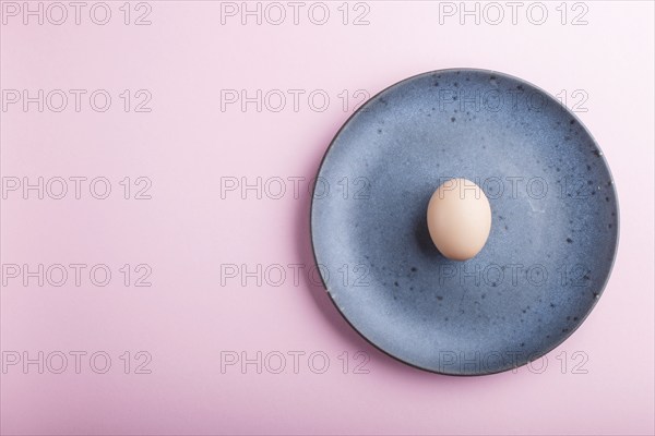 Raw uncooked single egg on a blue ceramic plate on a pink pastel background. top view, copy space