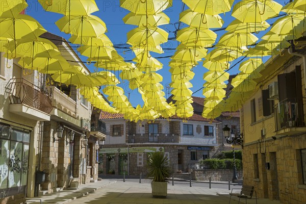 Street full of yellow umbrellas forming an artistic shadow installation under a blue sky and old buildings, Old Town, Los Molinos, Cuenca del Guadarrama, Madrid, Spain, Europe