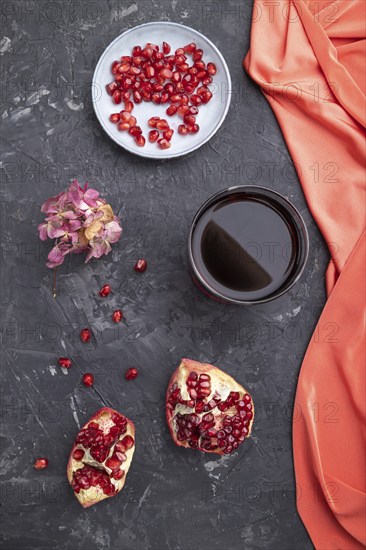 Glass of pomegranate juice on a black concrete background with red textile. Top view, close up, flat lay
