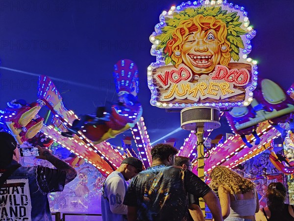 People in front of the illuminated carousel Voodoo Jumper at night, Cranger Kirmes, Herne, Ruhr area, North Rhine-Westphalia, Germany, Europe