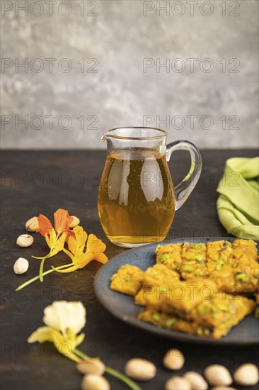 Traditional iranian dessert sohan with glass of green tea on a black concrete background and green textile. side view, close up, selective focus
