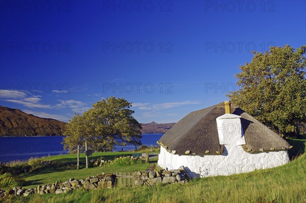 Small white house with thatched roof by the lake, surrounded by meadows and trees under a blue sky, Cottage, Holiday, Autumn, October, Hebrides, Isle of Skye, Hebrides, Scotland, United Kingdom, Europe