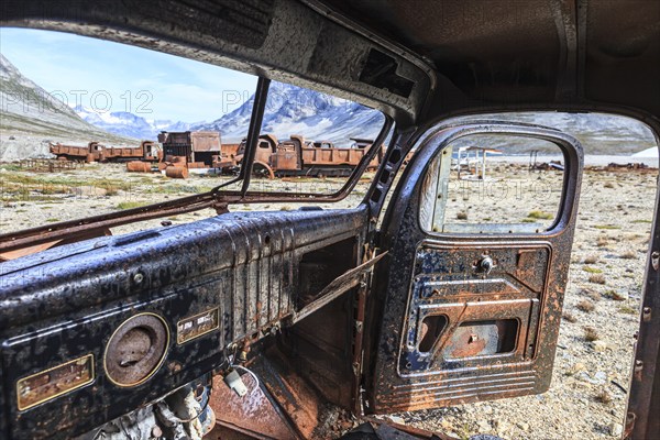 Interior view of a rusty car in front of steep mountains, remains of a US airbase from the Second World War, Ikateq Fjord, East Greenland, Greenland, North America
