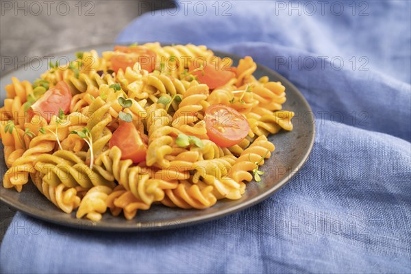 Tortiglioni semolina pasta with tomato and microgreen sprouts on a black concrete background and blue textile. Side view, close up, selective focus