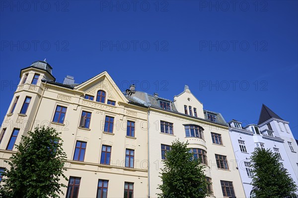 Historic Jugendstiel façade with large windows and trees in front under a clear blue sky, Bryggen, Bergen, Vestland, Norway, Europe
