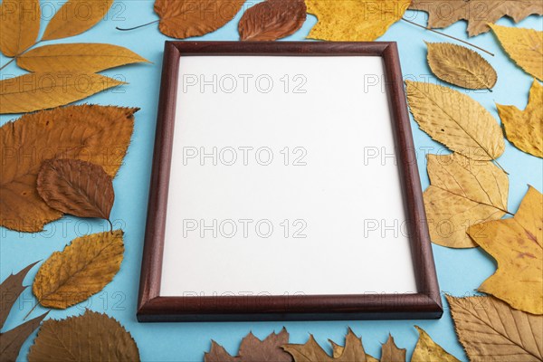 Composition with yellow and brown autumn leaves and wooden frame mockup on blue pastel background. Blank, side view, still life, copy space