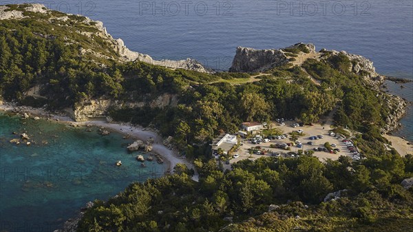 Car park and building in a rocky coastal landscape surrounded by trees and clear blue water, Anthony Quinn Bay, Vagies Bay, Rhodes, Dodecanese, Greek Islands, Greece, Europe