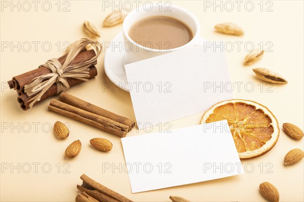 Composition of white paper business cards, almonds, cinnamon and cup of coffee. mockup on orange background. Blank, side view, still life, copy space