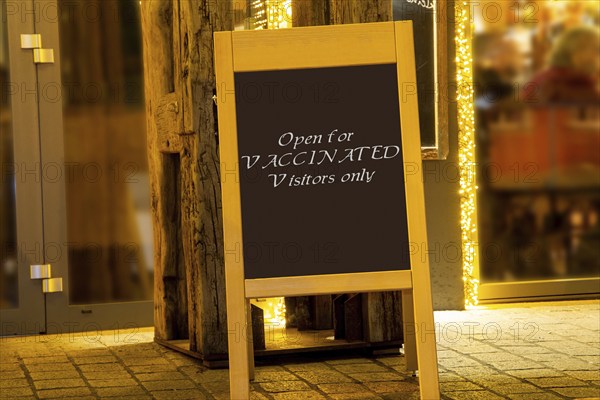 Street sign in front of a restaurant with the inscription Open for Vaccinated Visitors only (symbolic image, Composing)