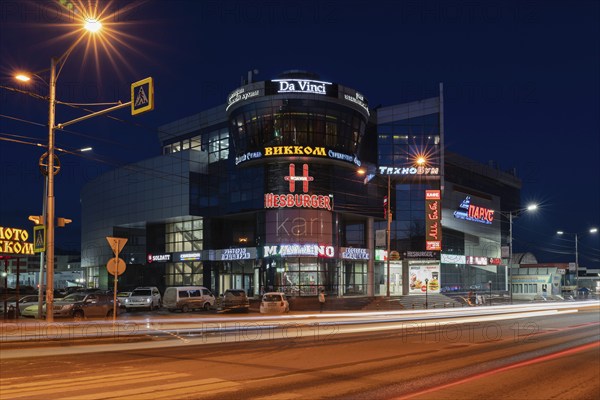 PETROPAVLOVSK CITY, KAMCHATKA PENINSULA, RUSSIA, 19 APRIL, 2018: Night view of building of shopping and entertainment center Sail and blurred traces of car headlights driving on central city road